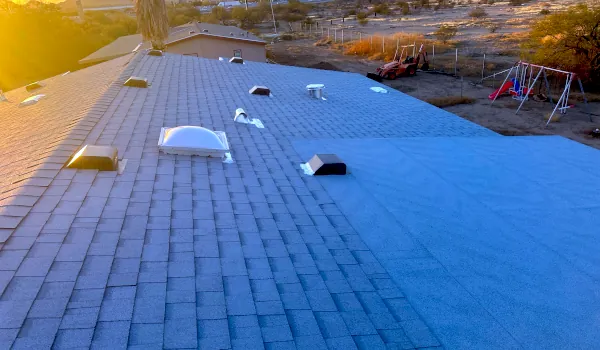 A shingled residential roof with vents and a skylight at sunset, viewed from above as a roof inspector evaluates the even rows of asphalt shingles.