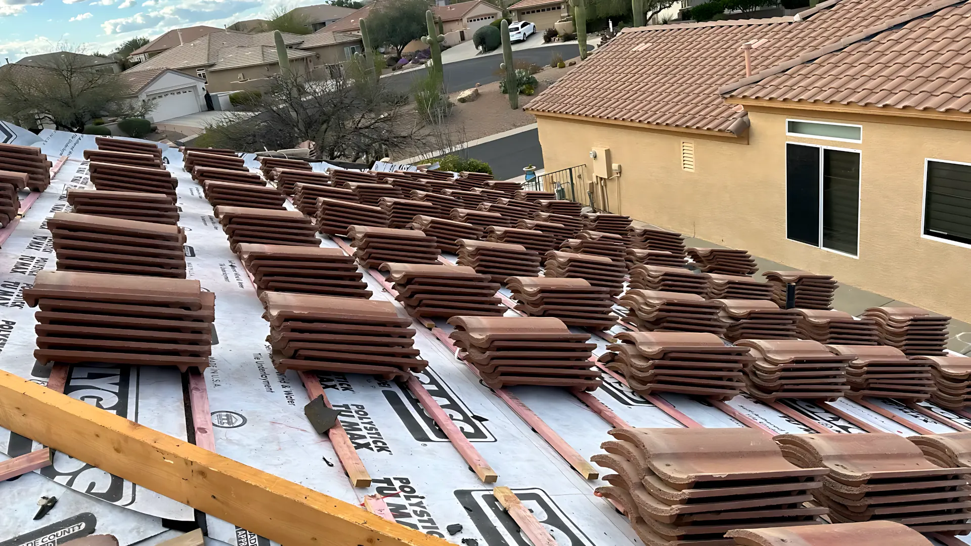 Stacks of terracotta tiles staged on underlayment across a roof during the roof installation process in Tucson.