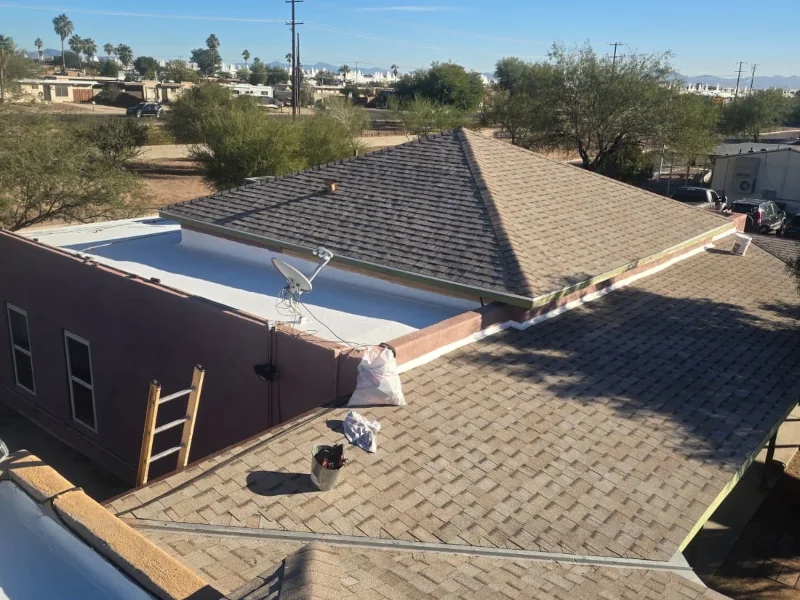 Roof inspection service of a low-angle view of adjoining tan-shingled roofs with a satellite dish, ladder, and small tools; desert trees and distant houses visible beyond.